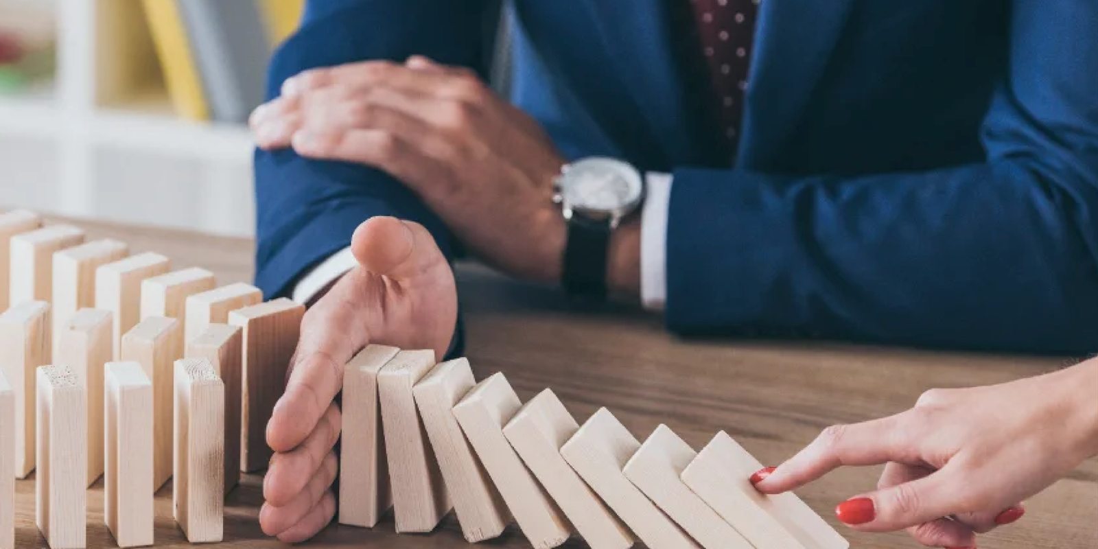 Mano que detiene la caída de fichas de dominó como representación de la gestión de riesgos ISO 31000